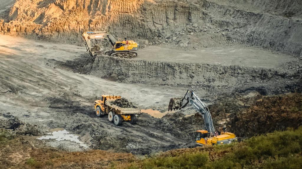 A photo of three large yellow construction vehicles working in an enormous open grey pit.